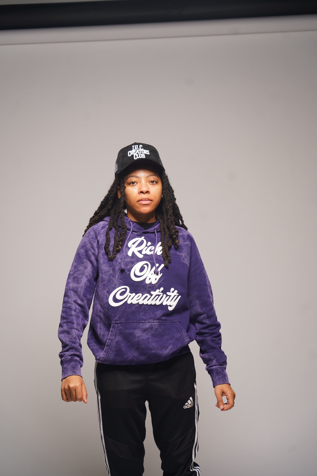 Woman wearing the purple Rich Off Creativity hoodie and Lu.C. Creators Club hat