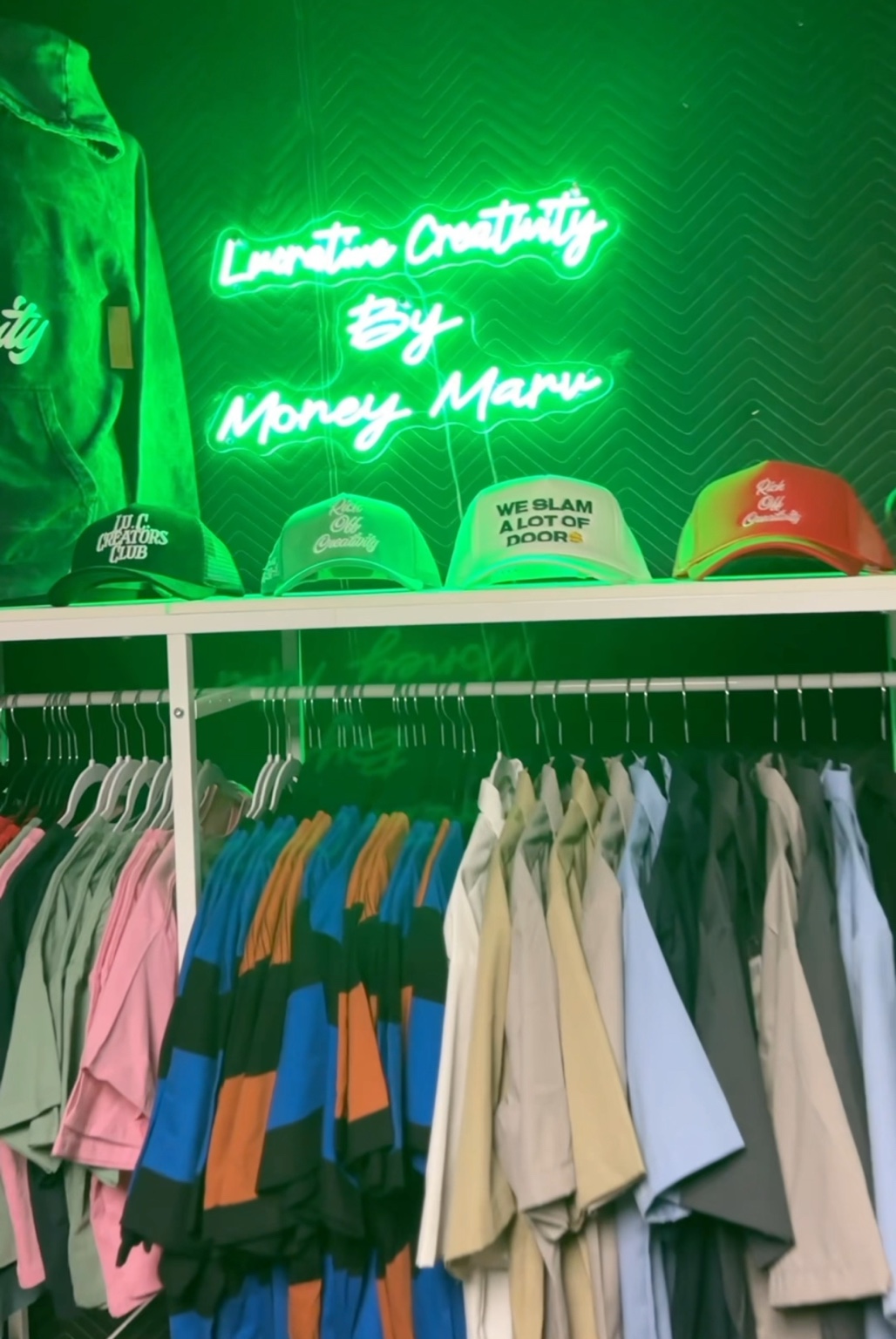 Lu.C. clothing range displayed beneath the green Lucrative Creativity neon sign