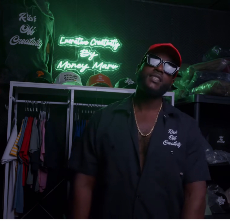 Creative wearing a Rich Off Creativity work shirt in front of the Lucrative Creativity neon wall