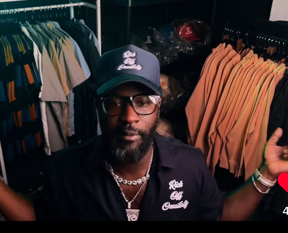 Creative wearing a Rich Off Creativity work shirt and cap between the Lu.C. clothing racks